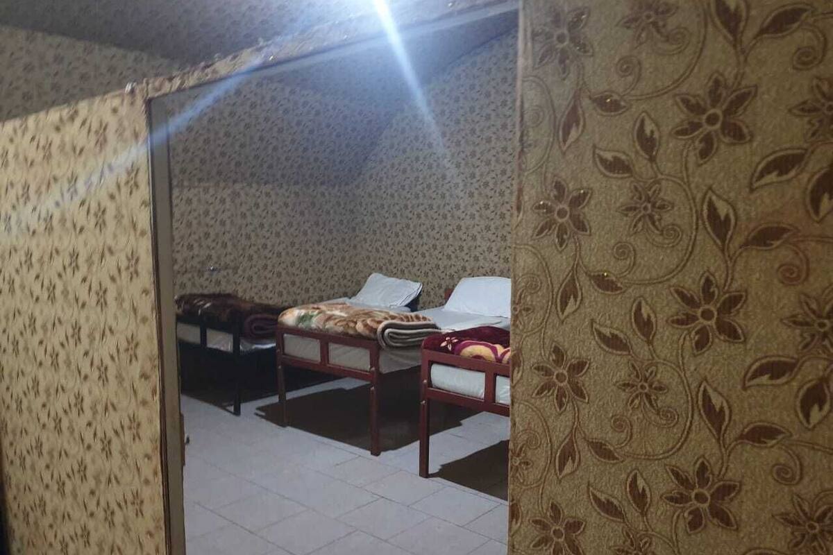 A room with two wooden beds, a tiled floor, and floral-patterned wallpaper.