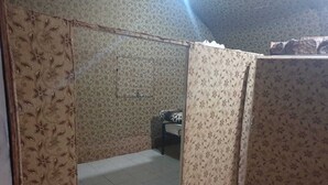 A small, dimly lit room with floral wallpaper, a bed with a patterned bedspread, and a visible door. - Wadi Rum Desert Camp (Wadi Rum)