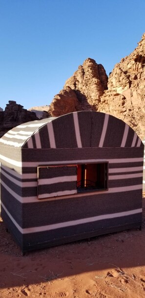 A small, striped, tent-like structure with a window, set against a rocky desert backdrop. - Wadi Rum Desert Camp (Wadi Rum)