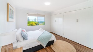 A bedroom with a bed, a window with a view, a wardrobe, and a bedside lamp. - Ocean Dreaming - Brooms Head (Brooms Head)