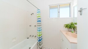 Une salle de bain avec une baignoire, un rideau de douche, une fenêtre et un lavabo agrémenté d’une plante.