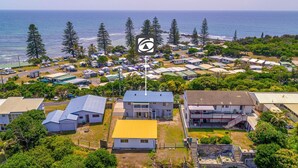 An aerial view of a coastal campground with multiple RVs and cabins, a flagpole with a logo, and a clear view of the ocean. - Ocean Dreaming - Brooms Head (Brooms Head)