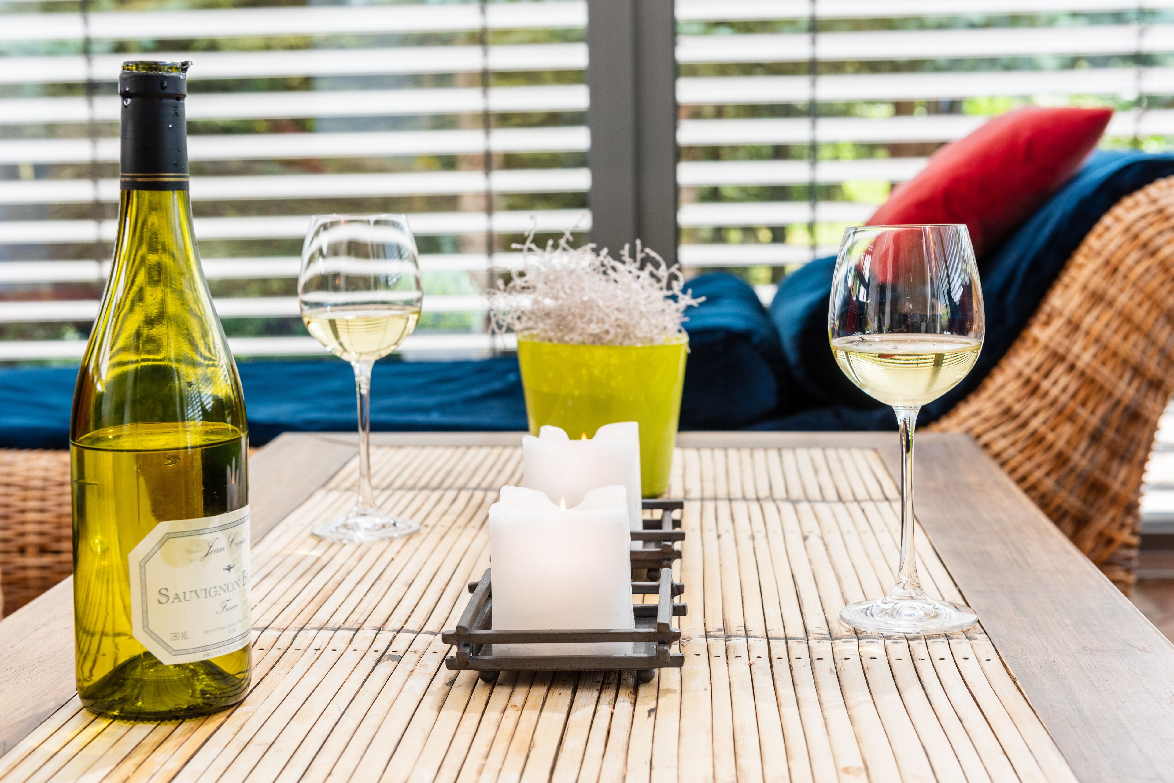 Una botella de vino sauvignon, dos copas de vino, una vela y un candelabro decorativo sobre una estera de bambú.