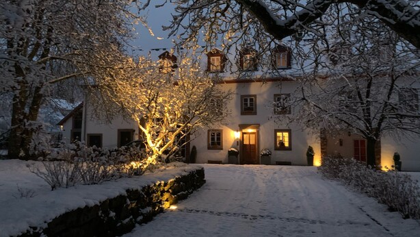 A snow-covered building with a well-lit entrance and a pathway leading to it.