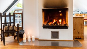 A fireplace with a visible fire, a wooden chair, and three lit candles.