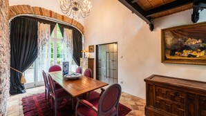 A dining area with a wooden table, red chairs, a chandelier, and a stone wall.