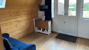Una habitación con paredes de madera, un sofá azul, un escritorio con una computadora y una puerta con señal de salida de incendios.