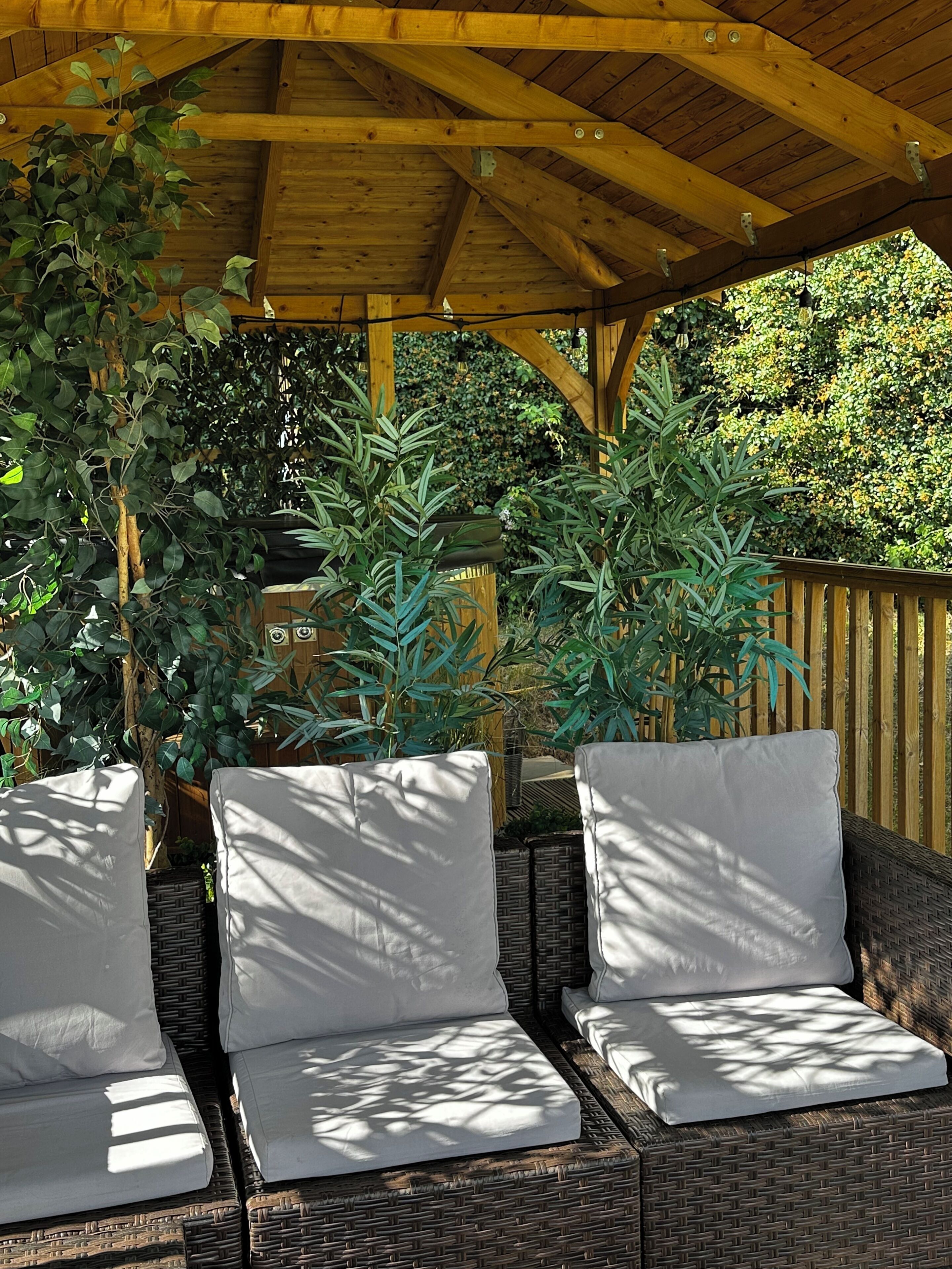 Un espace extérieur aménagé, abrité et doté de mobilier en osier et de plantes en pot.