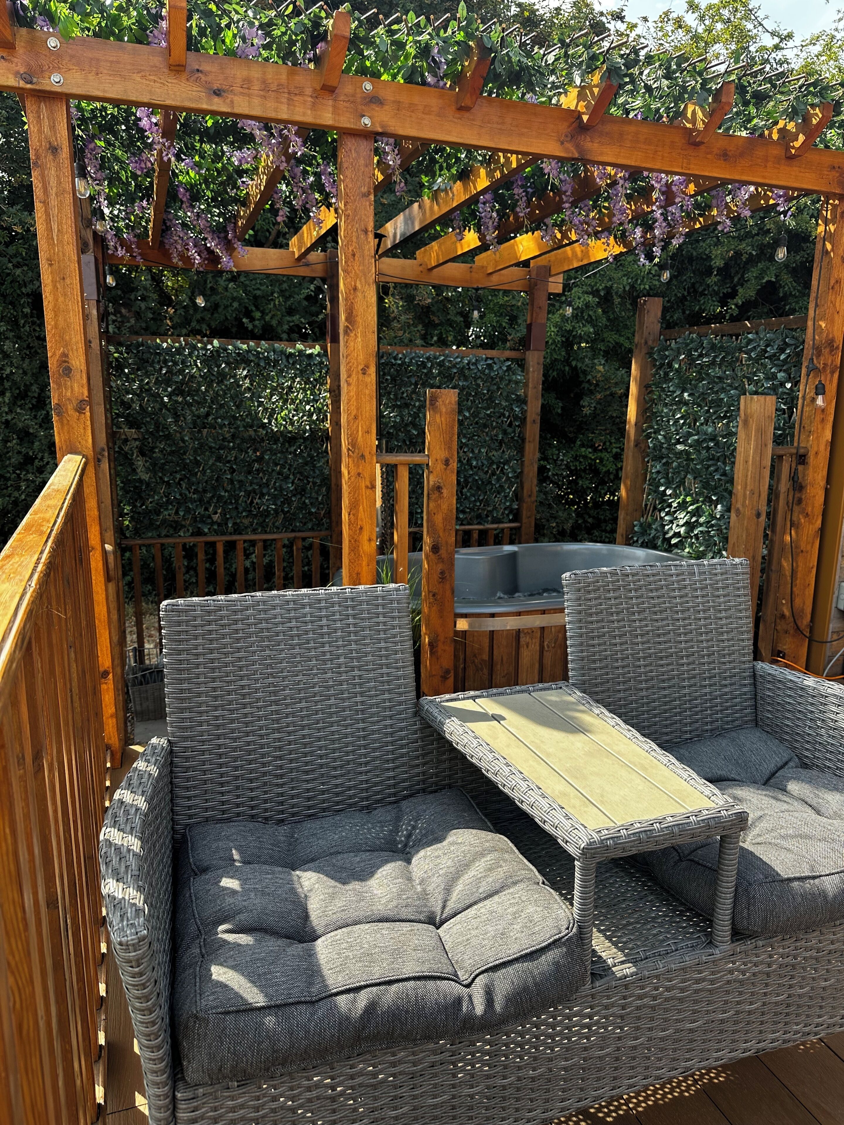 Una pergola in legno con un’area salotto arredata con mobili in vimini e un tavolo integrato.
