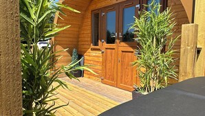 Una cabaña de madera con techo curvo, una puerta de madera con el cartel "Daisy" y un pequeño porche con plantas.