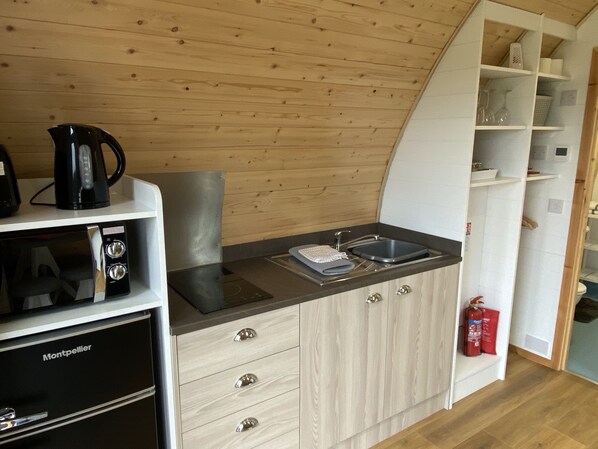 Una cocina compacta con microondas, hervidor y fregadero.