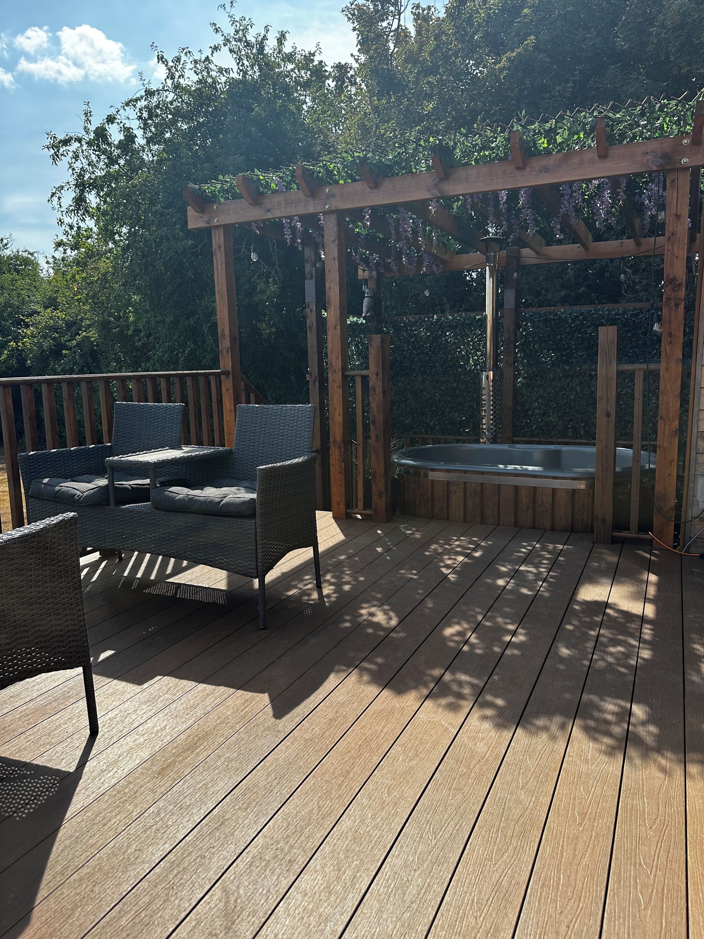Een houten terras met tuinmeubilair, een jacuzzi en een pergola met hangende lichten.