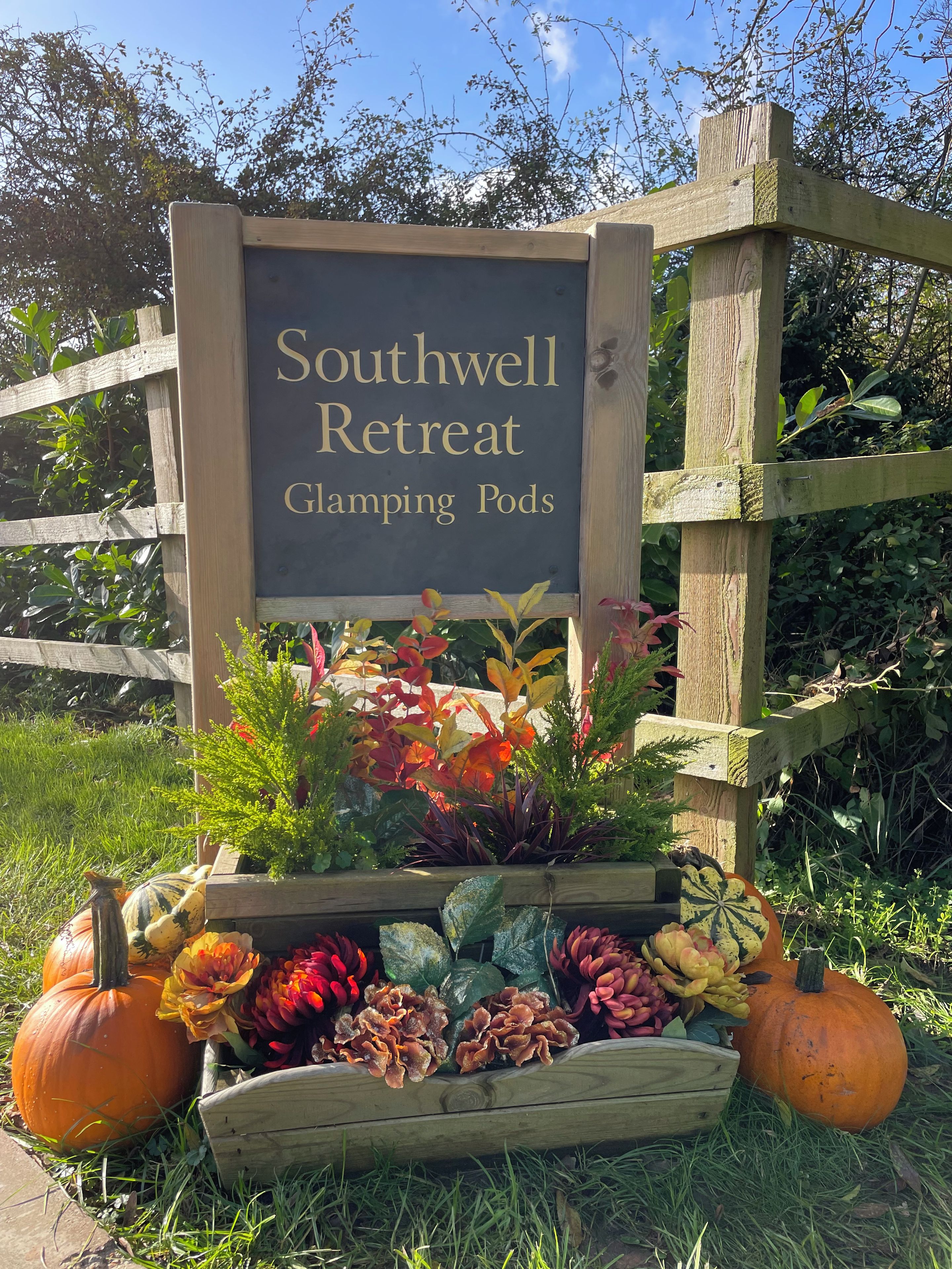 Un letrero para Southwell Retreat, con una cerca de madera y un macetero con flores de otoño y calabazas.