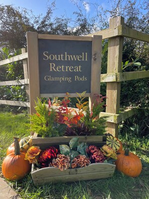 Un letrero para Southwell Retreat, con una cerca de madera y un macetero con flores de otoño y calabazas.