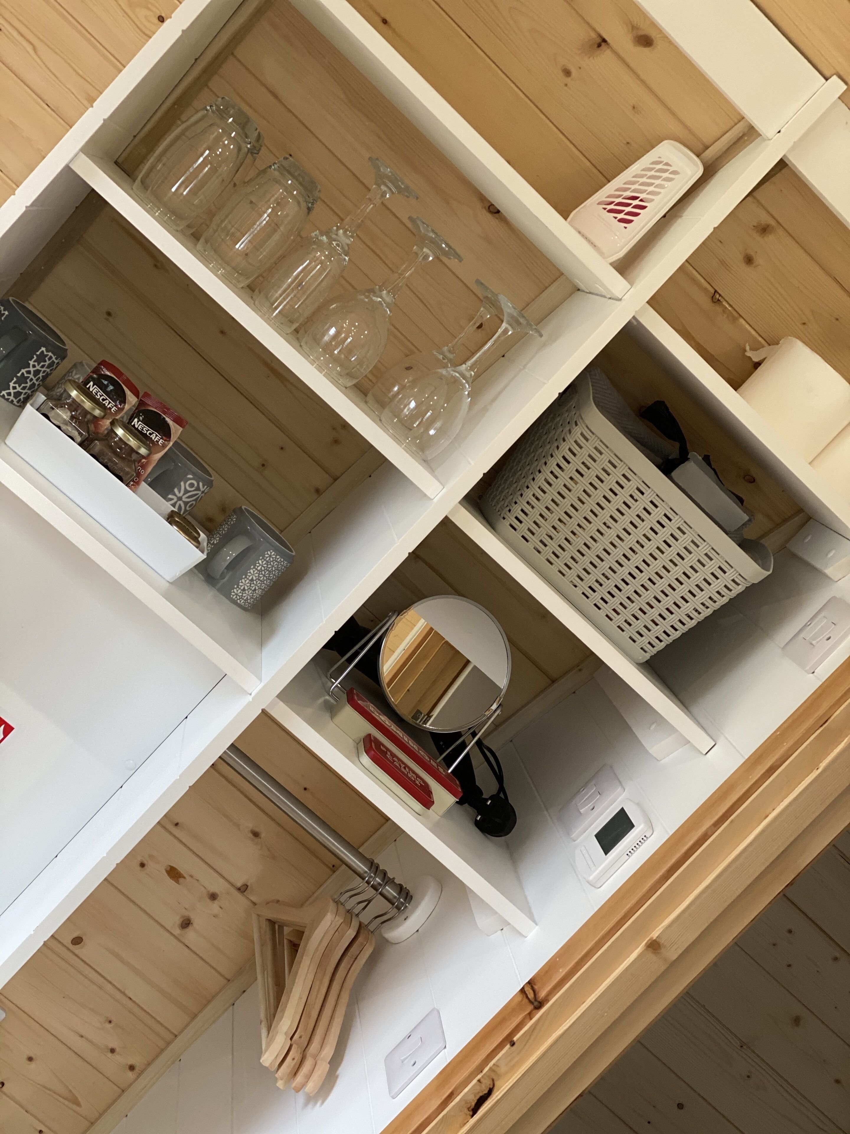 A neatly organized shelf with various items including glassware, jars, and a small mirror.