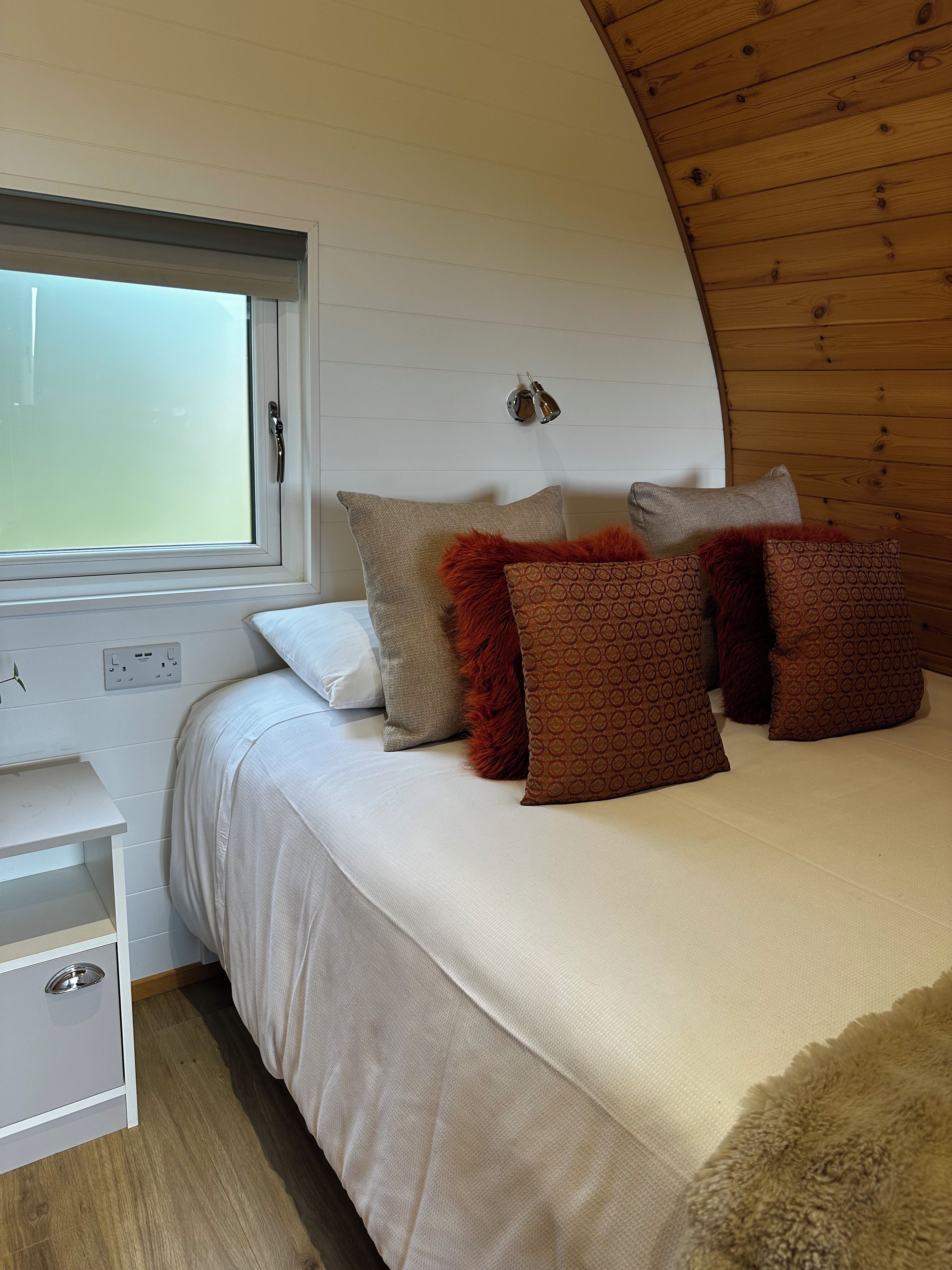 Quarto com cama, almofadas, mesa de cabeceira e janela.