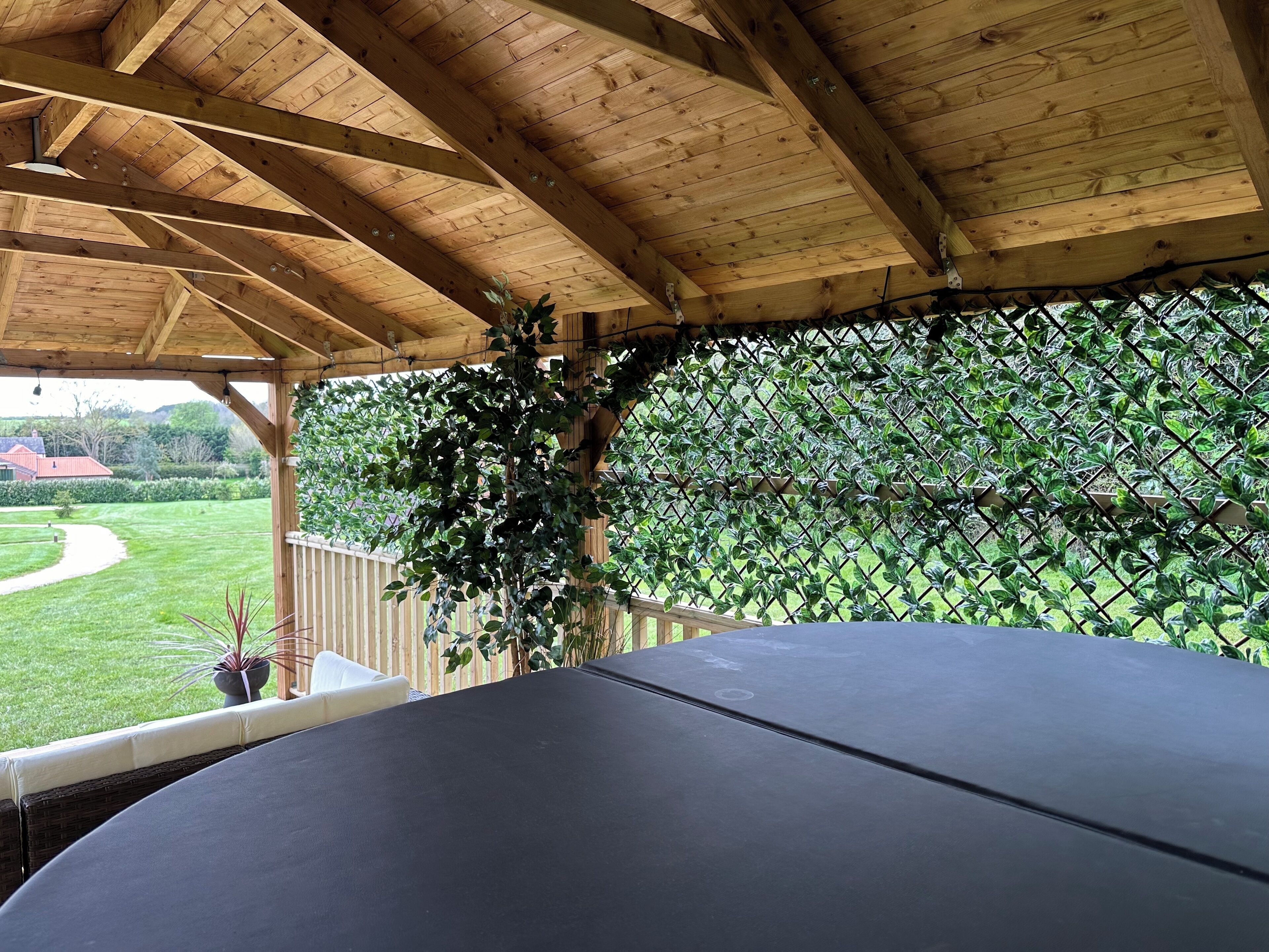 Un espace extérieur abrité, aménagé pour s’asseoir, avec vue sur un jardin et une maison en arrière-plan.