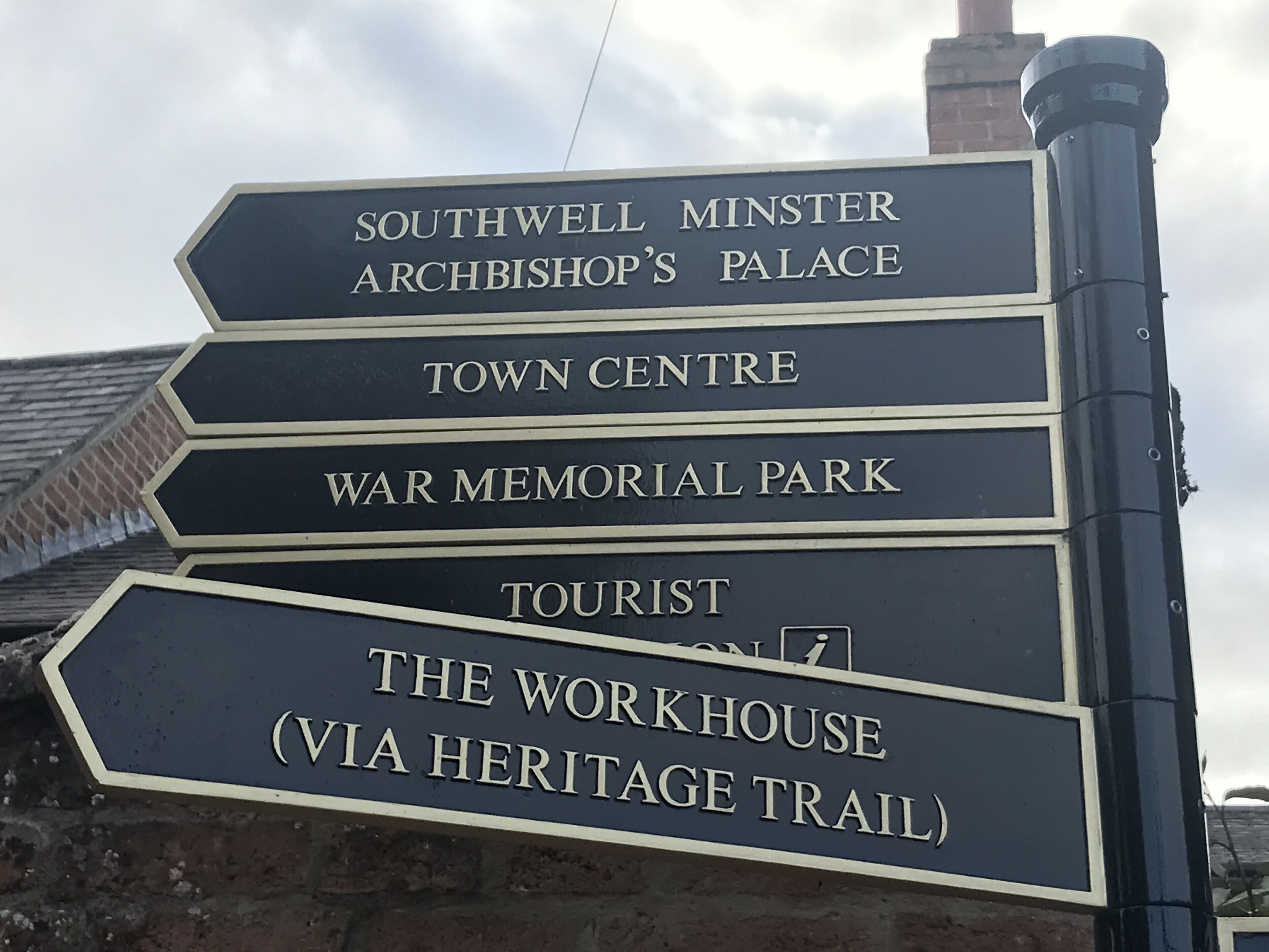 En skiltepeger med flere pile, der viser vejen til forskellige destinationer, herunder Southwell Minster, bymidten, War Memorial Park, Turistinformation og The Workhouse.