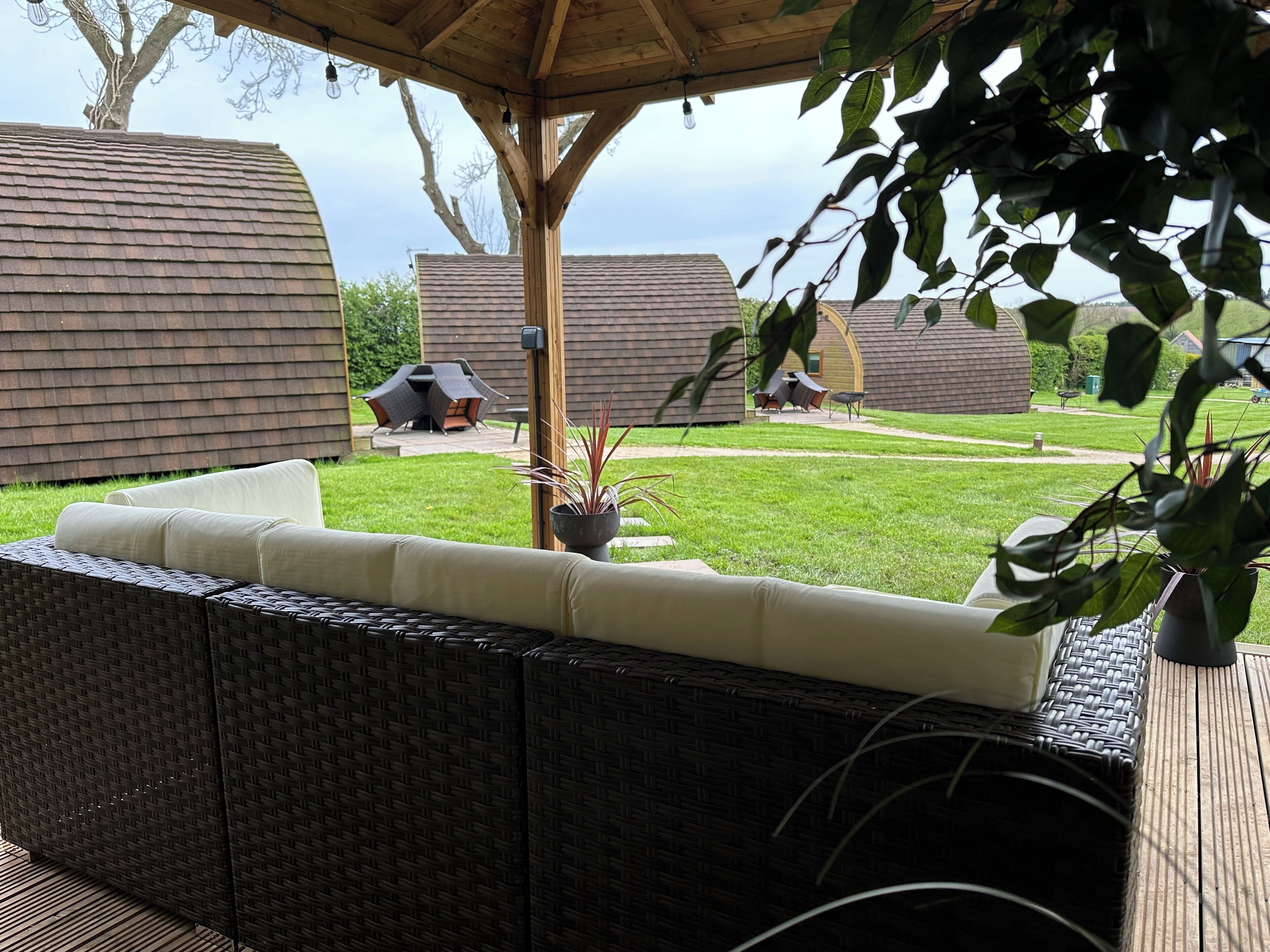 A covered outdoor seating area with wicker furniture and a view of a backyard with a barbecue and a lawn.