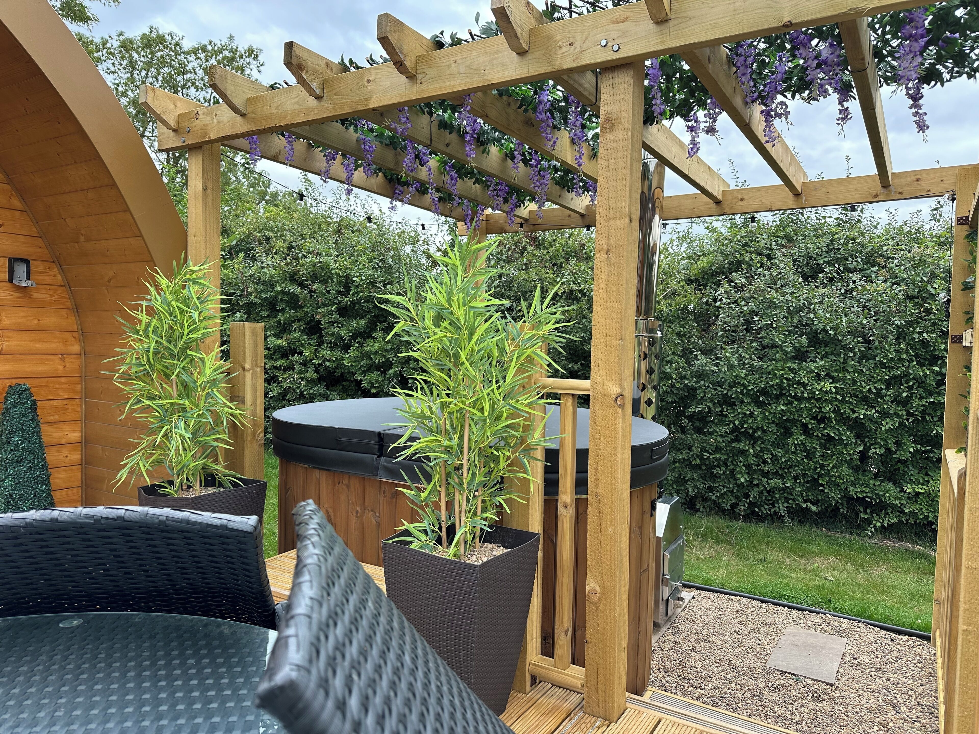 A wooden pergola with purple flowers, a hot tub, and potted plants.