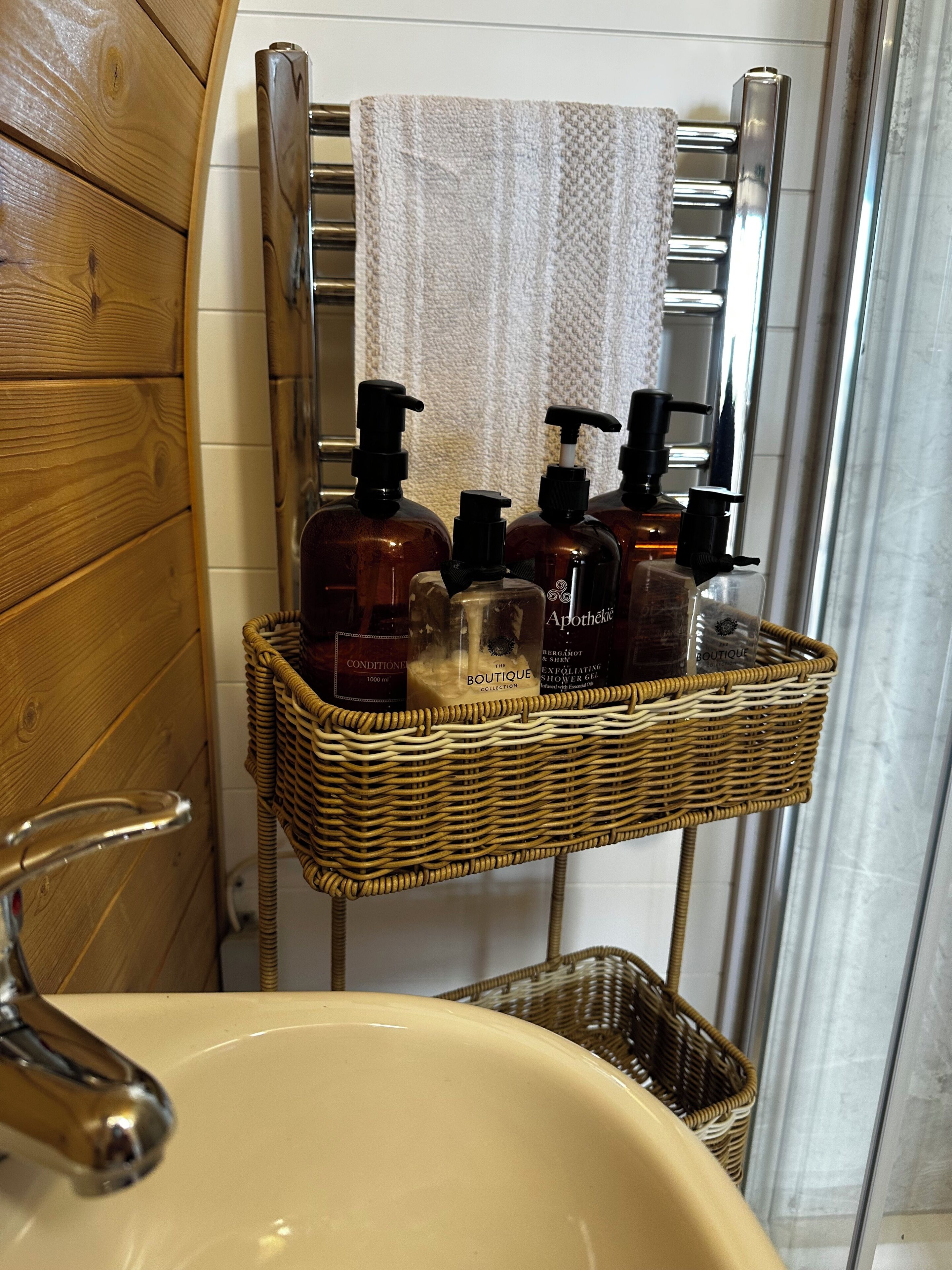 A bathroom with a wooden vanity, a white sink, and a wicker shelf holding toiletries.