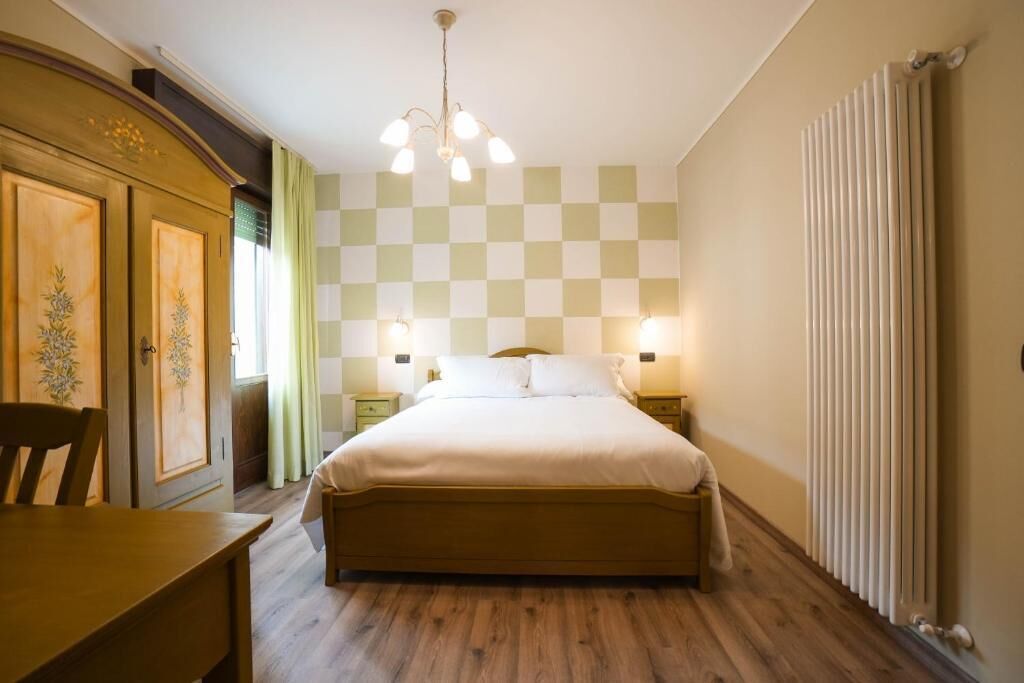 Ein Schlafzimmer mit karierter Wand, einem hölzernen Bett, Nachttischlampen, einem Heizkörper und einem Holzschrank.