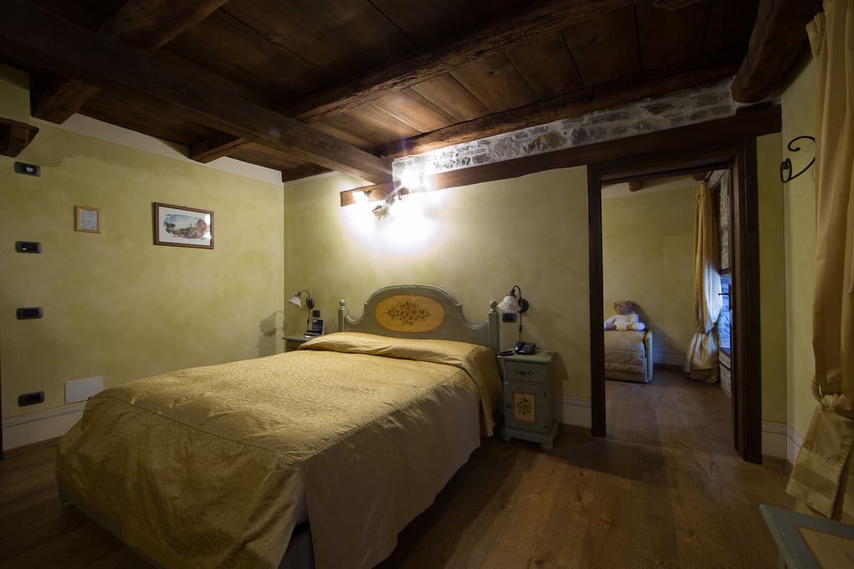 Ein Schlafzimmer mit Holzbalkendecke, einem Bett mit Kopfteil, Nachttischen und einem Spiegel.