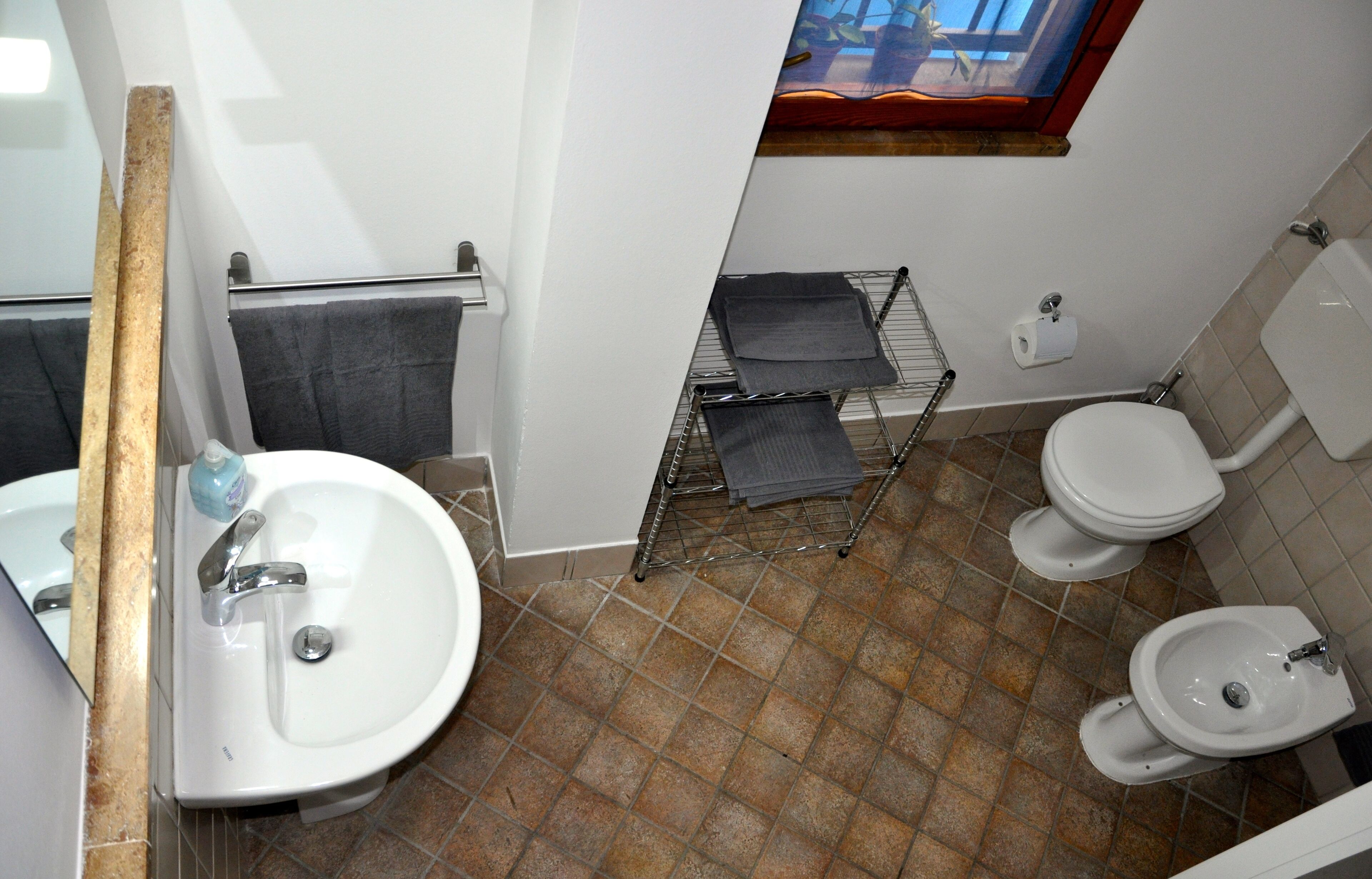 Une salle de bain équipée d’un lavabo, de toilettes et d’un bidet. On y trouve également un porte-serviettes et une tringle pour le rideau de douche.