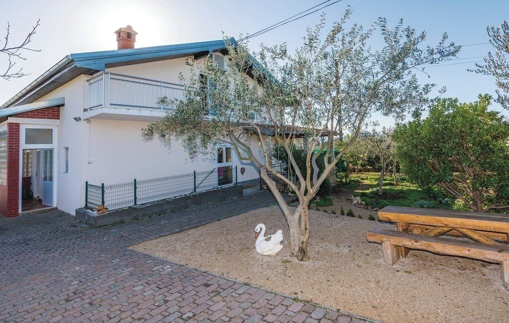 A two-story house with a balcony, a tree, and a swan statue in the yard.