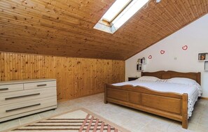Un dormitorio con techo de madera, una cama, un aparador y un tragaluz.