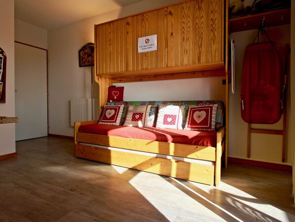 A wooden bunk bed with a sign above it, a red bag hanging on a hook, and a radiator on the wall.