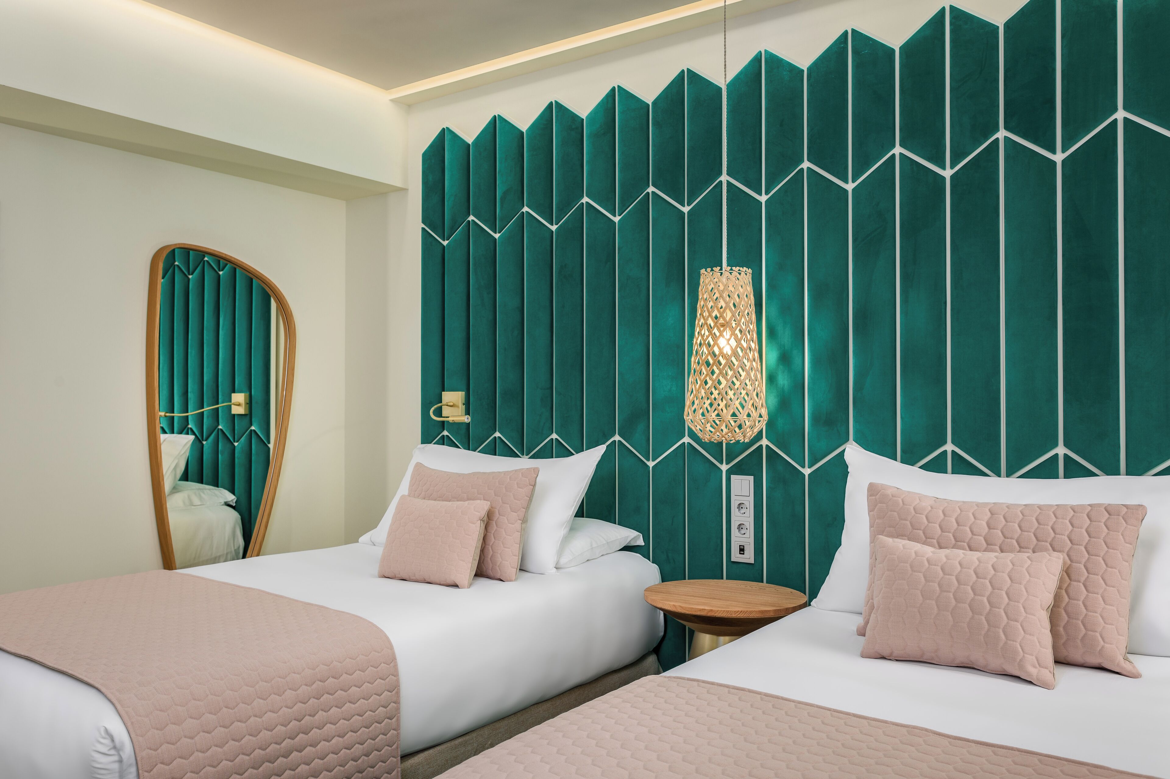 Habitación de hotel con dos camas, un espejo, pared verde con textura y una lámpara colgante.
