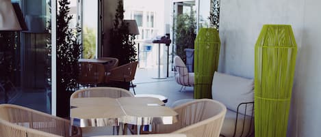 Un espacio exterior moderno con sillas de mimbre, una mesa redonda, puertas de cristal que dan a un balcón y una maceta cilíndrica verde.