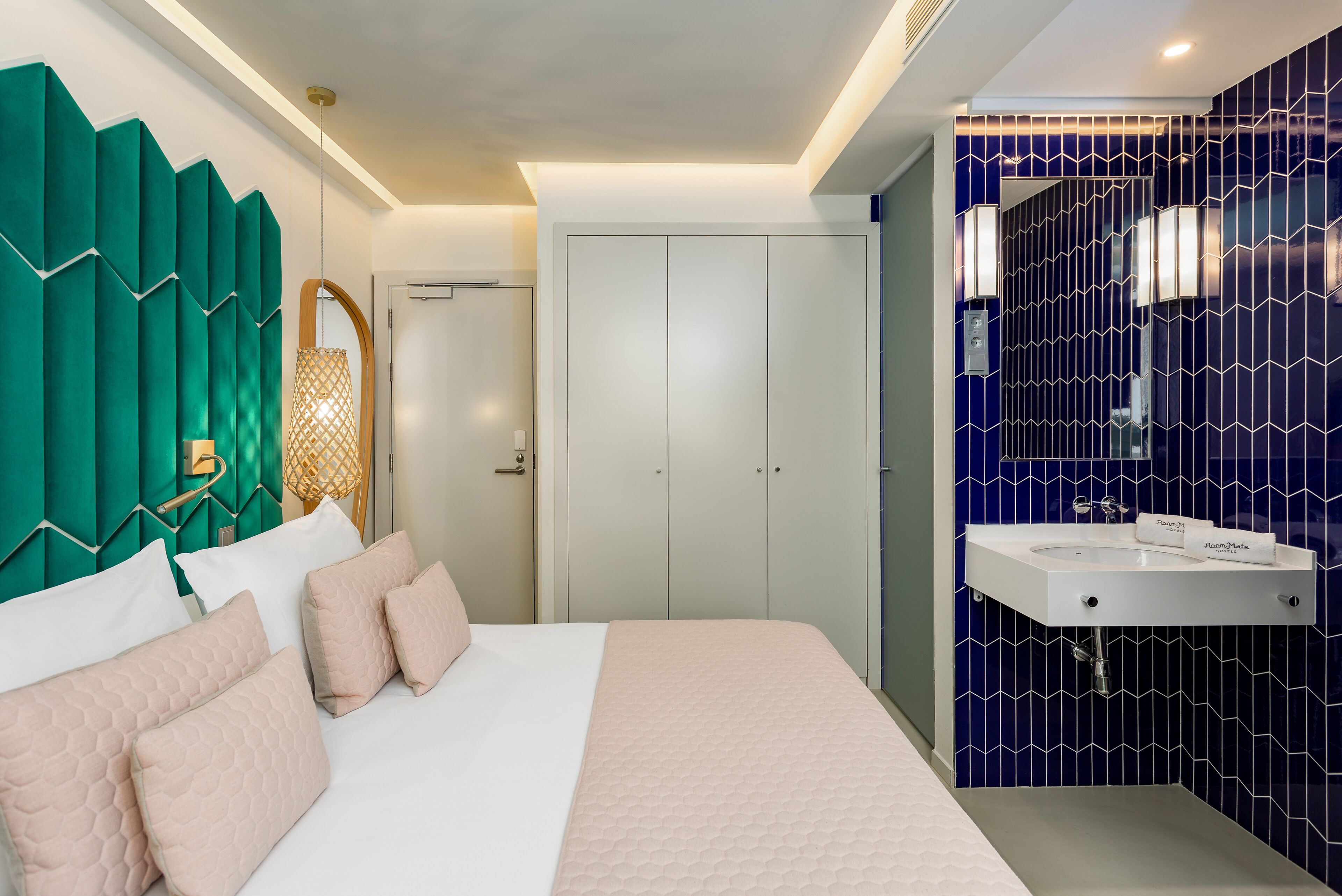 Une chambre moderne avec un grand lit, une armoire et une salle de bain dont un mur est recouvert de carreaux bleus et qui est équipée d’un lavabo blanc.