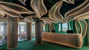 A modern interior with unique wooden ceiling structures, a reception desk, and a view of the city.