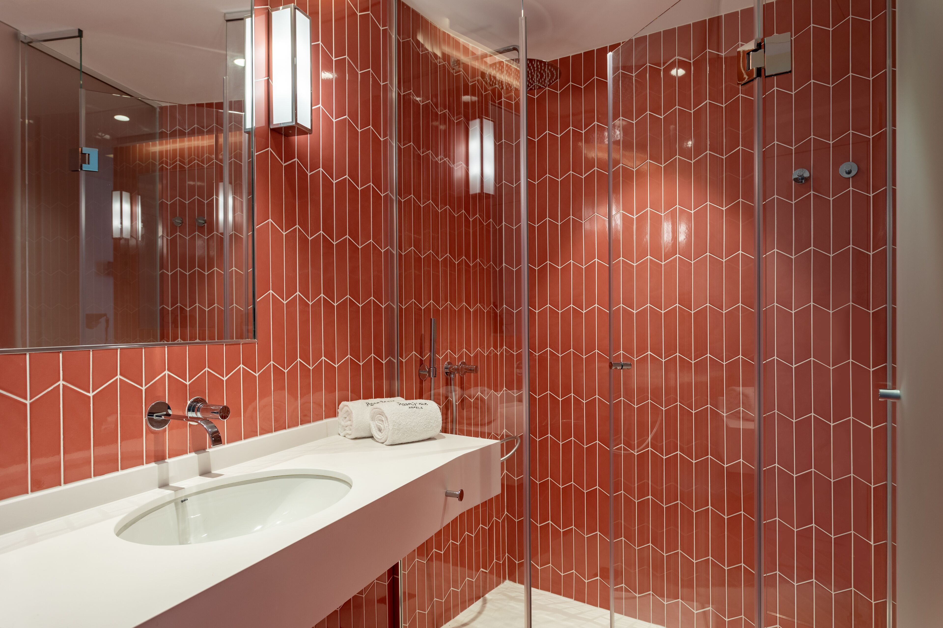 Ein modernes Badezimmer mit einem großen Spiegel, zwei Waschbecken und einer Duschkabine mit rot gemusterten Wand.