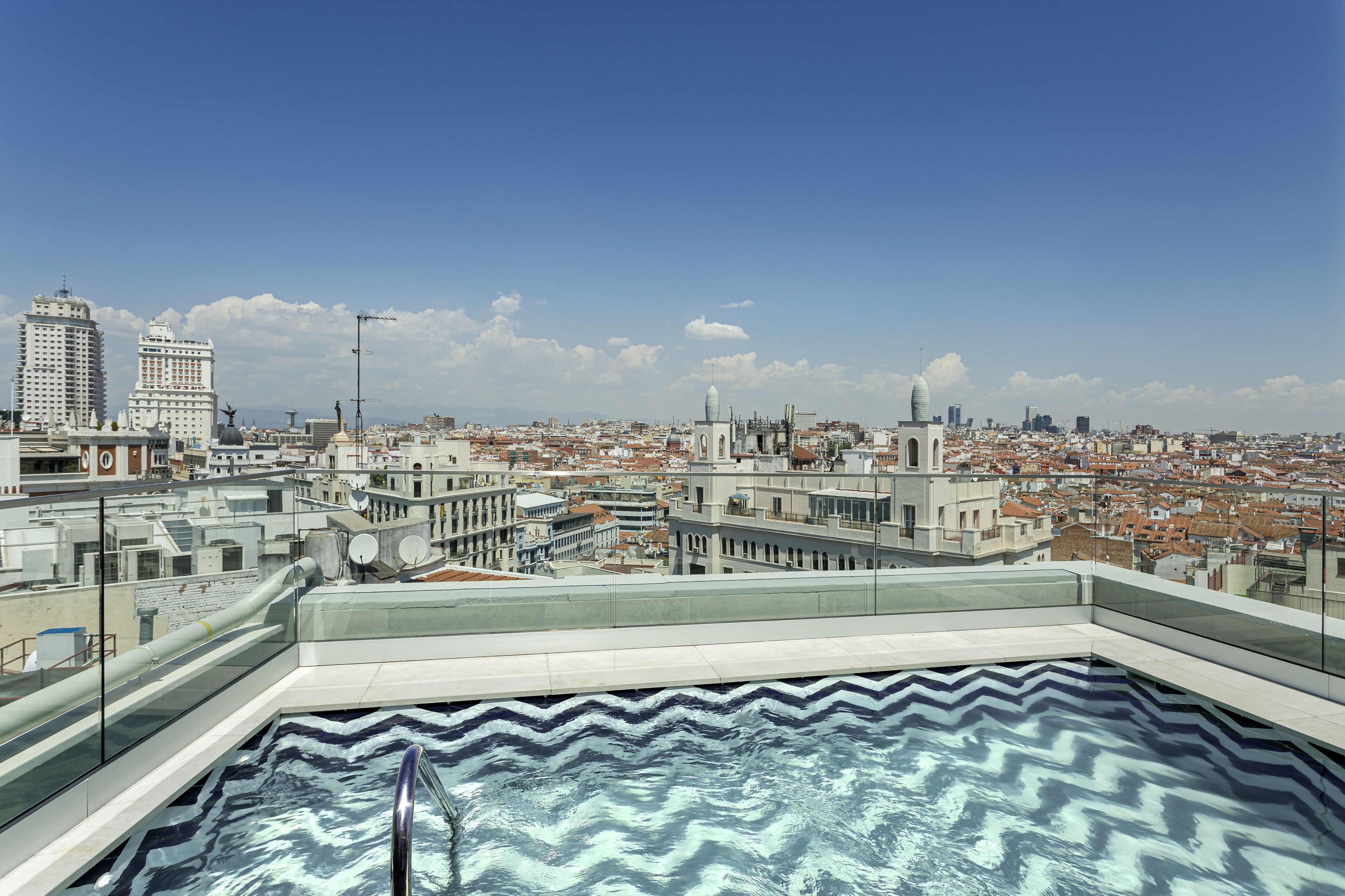 Una piscina en la azotea con vista a un paisaje urbano, con edificios modernos y un cielo despejado.