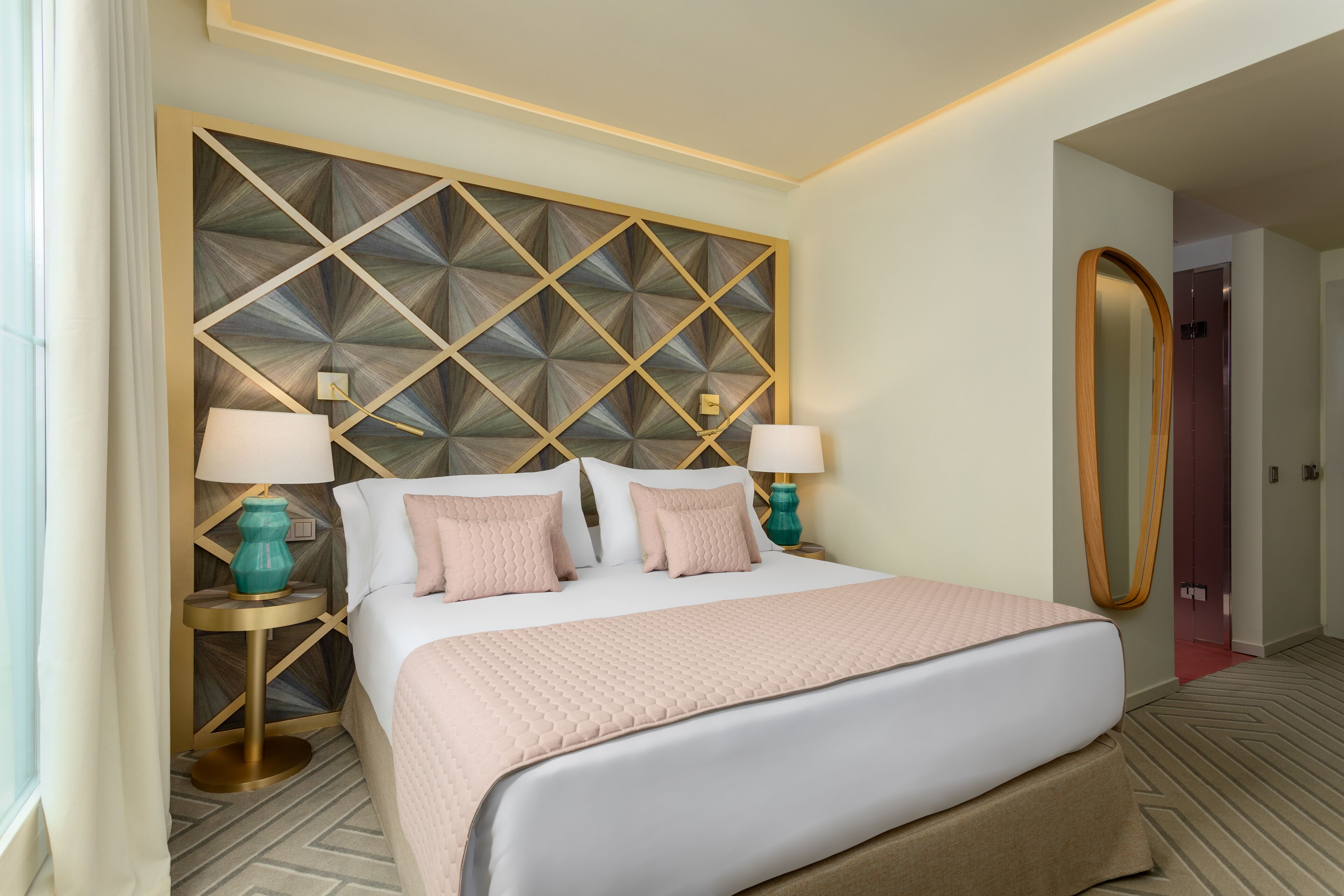 Une chambre d’hôtel avec un grand lit, deux tables de chevet avec des lampes, un panneau décoratif au mur et un grand miroir.