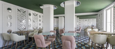 A modern dining area with round tables and chairs, patterned floor tiles, and decorative wall panels.