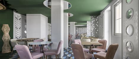 A modern interior with geometric patterned flooring, round tables, and pink upholstered chairs.