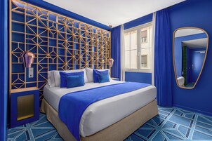 Ein modernes Hotelzimmer mit Wand im geometrischen Muster, einem großen Bett mit blauer Bettwäsche und einem gro ßen Spiegel.