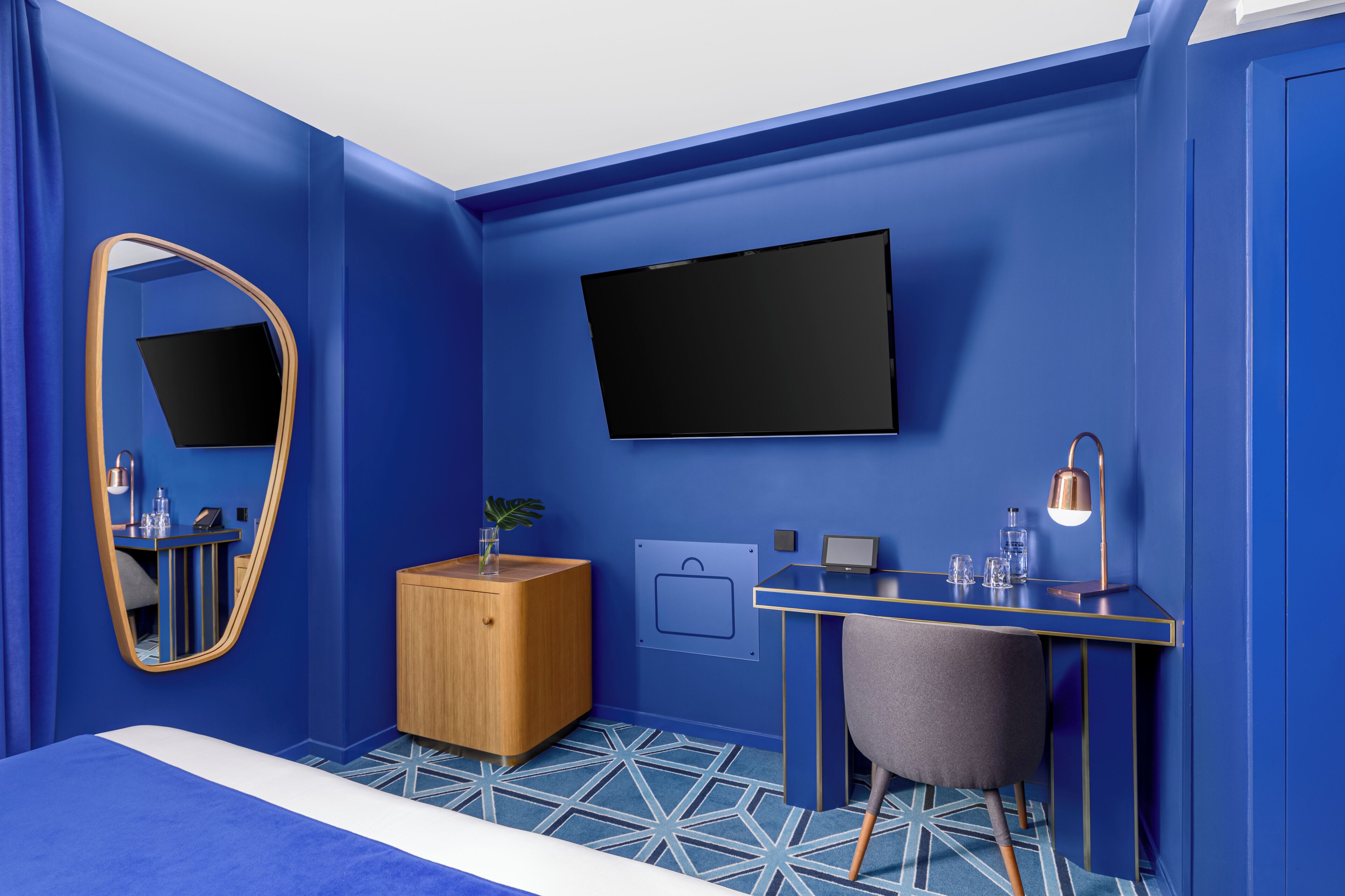 Un dormitorio moderno con una cama grande, un escritorio con silla, un televisor, un espejo y un pequeño armario de madera.
