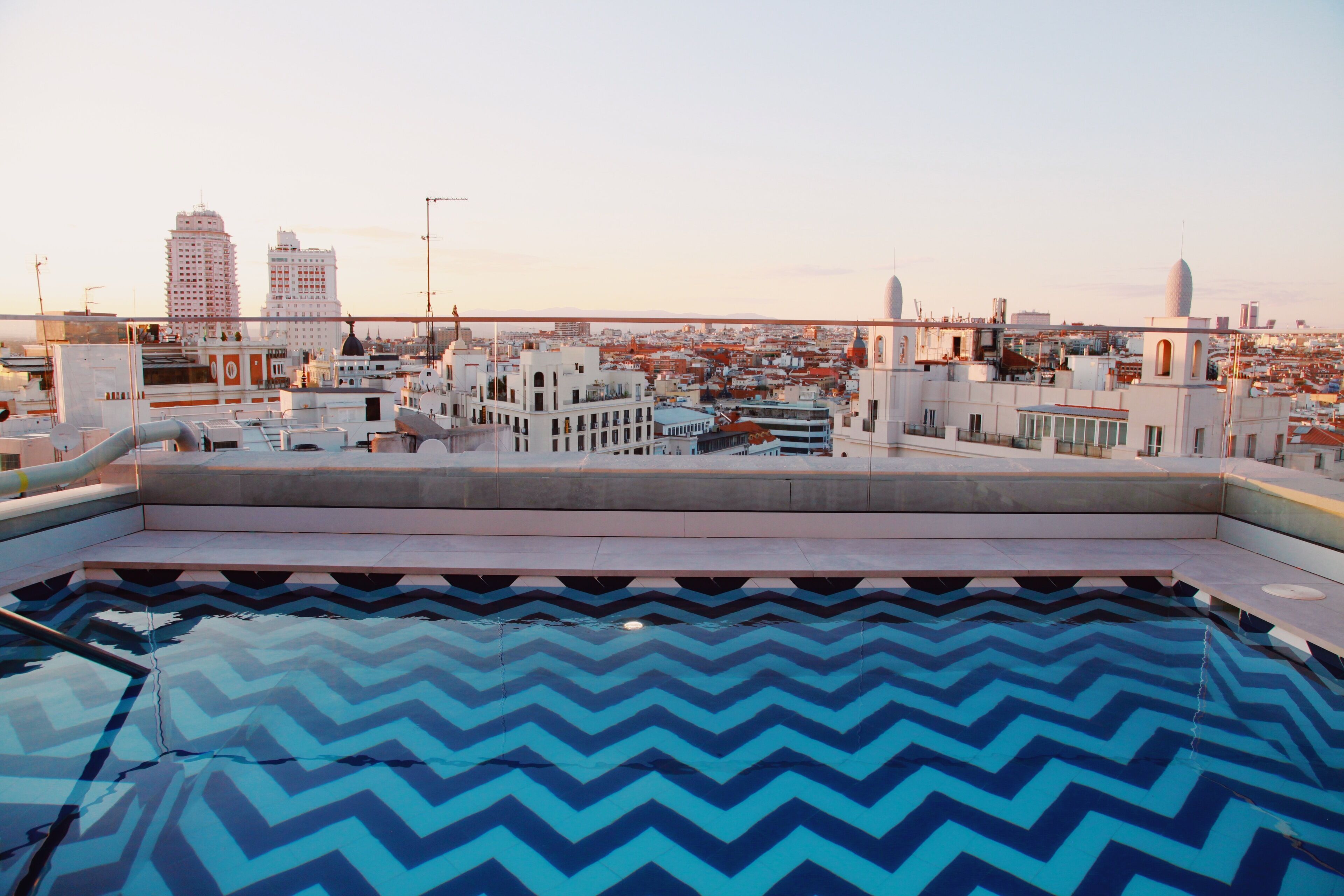 Una piscina en la azotea con un diseño de vivos en el suelo, rodeada de edificios con una mezcla de estilos arquitectónicos.
