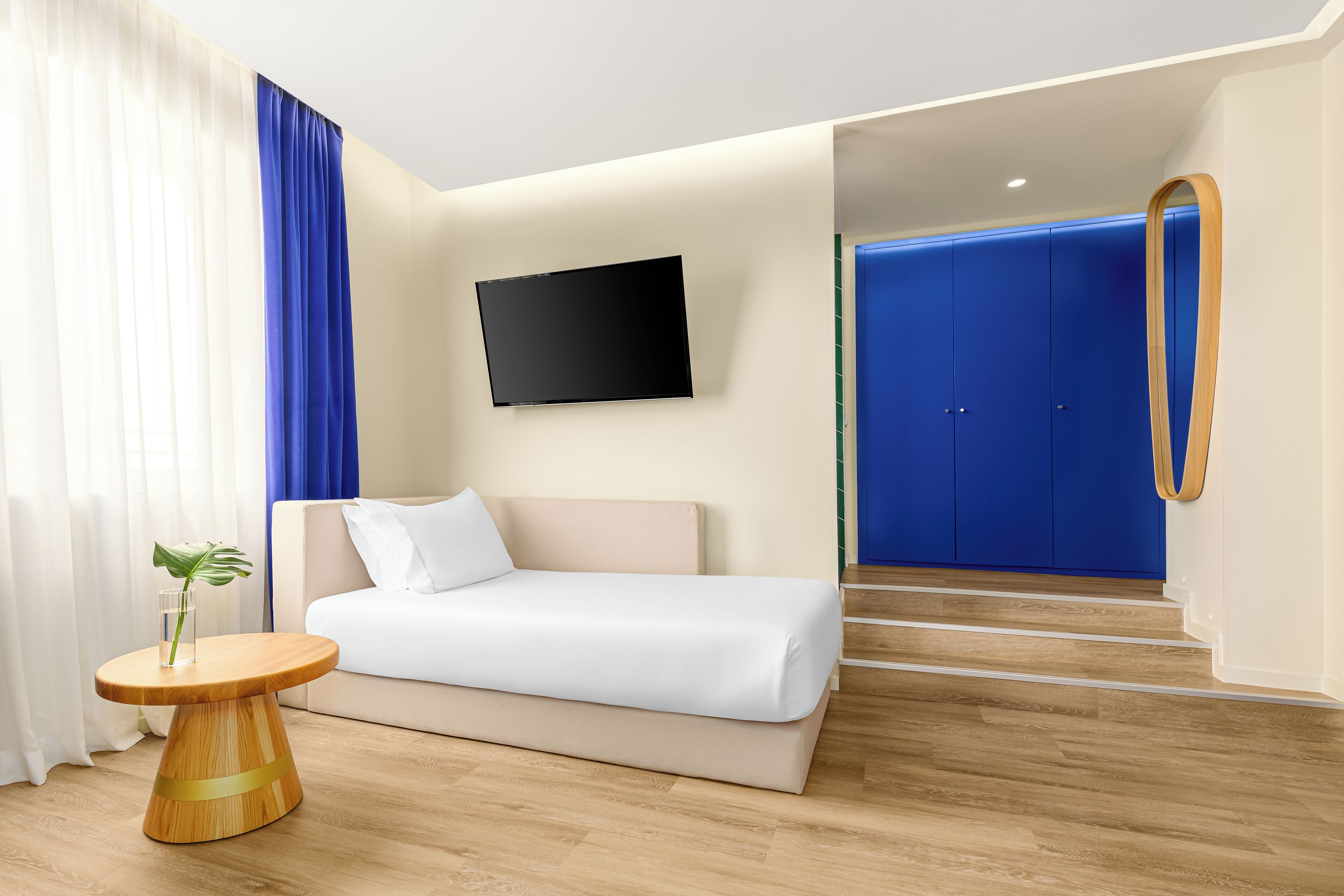Habitación de hotel moderna con cama, televisión montada en la pared y una puerta azul.
