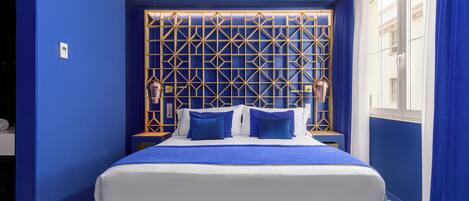 A hotel room with a large bed, blue walls, and a geometric patterned headboard.