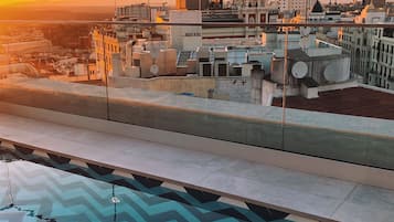 A rooftop terrace with a chevron-patterned floor, overlooking a cityscape at sunset.