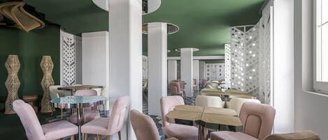 Un interior moderno con mesas redondas y sillas rosas, techo verde y baldosas de suelo con motivos.