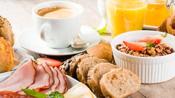 Ein reichhaltiges Frühstücksbuffet mit Kaffee, Saft, Brot, Schinken und einer Schüssel Granola.