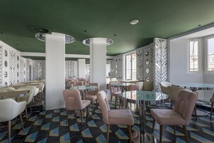 Un interno di ristorante moderno con tavoli e sedie rotonde, pareti verdi e pavimento con piastrelle decorate.