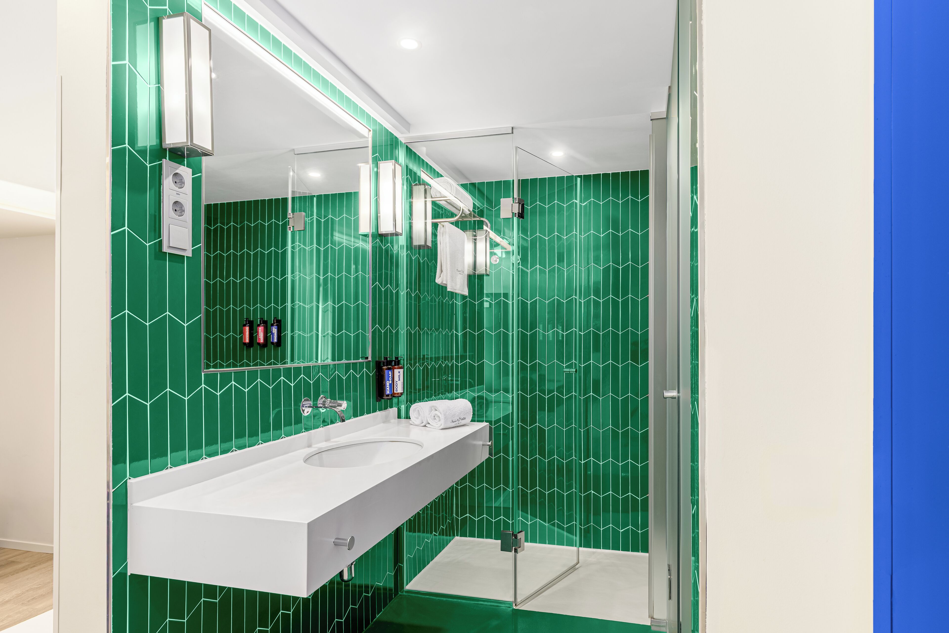 Een moderne badkamer met een wit wastafeltje, een grote spiegel en een douche.